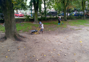 Dzieci grabiące liście i zbierające je na taczkę