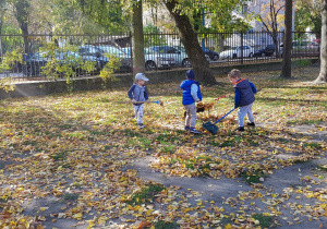 Chłopcy grabiący liście i wrzucający na taczkę